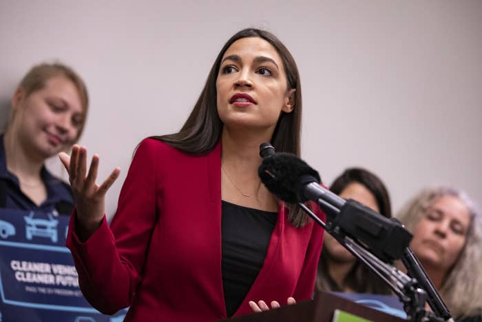 Alexandria Ocasio-Cortez gestures with her hands as she speaks into a microphone at a press conference.