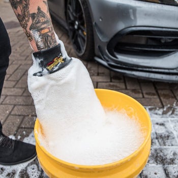 The car washing mitt on a person's hand being dipped into a bucket of soapy water
