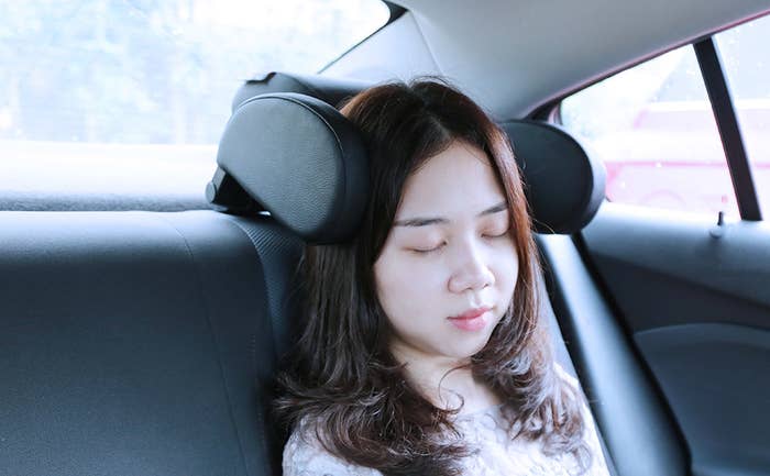 A person sleeping in the car with two headrest bumpers on either side of their head