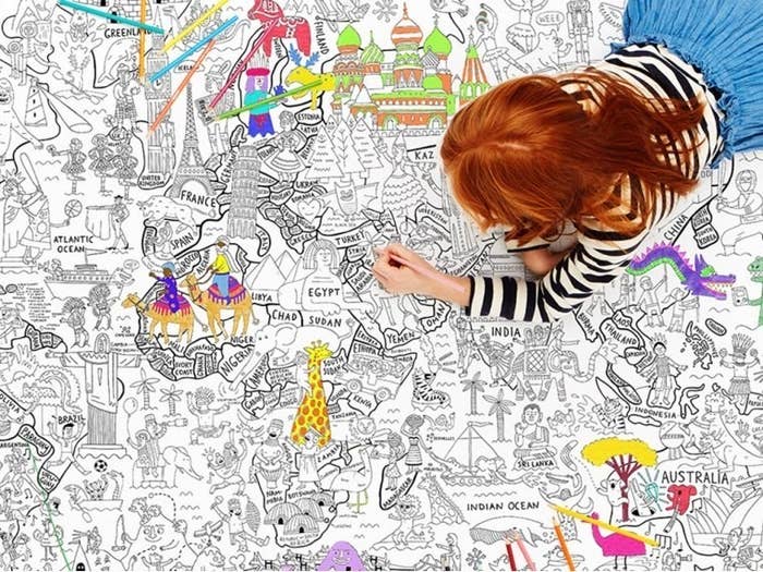 A kid lying on the around the world themed poster and coloring it