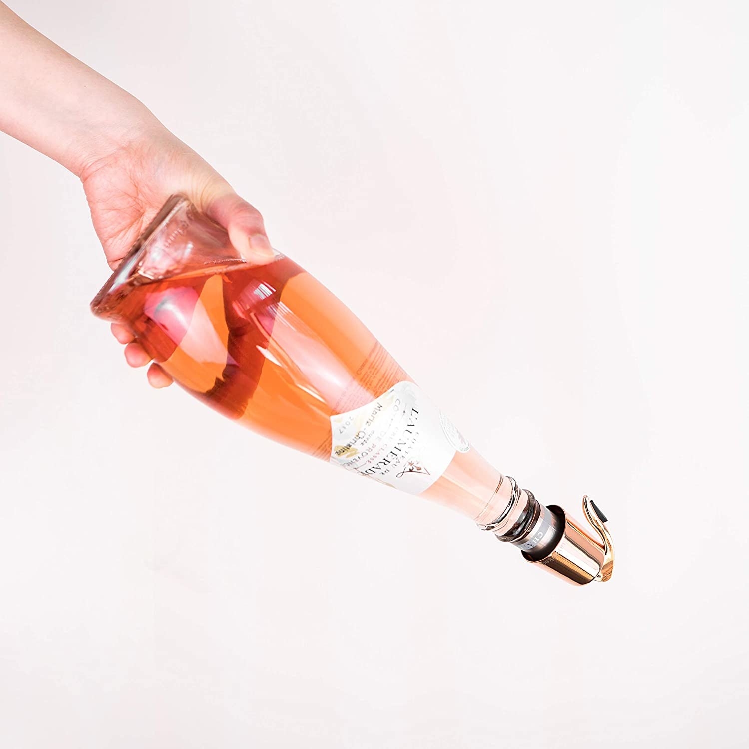 A person holding a bottle of rosé with a rose gold wine stopper on it