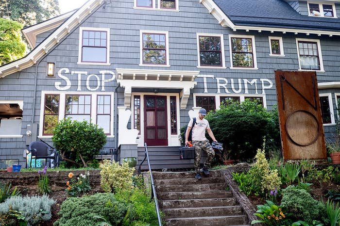 Man walks down the stairs of a house with the words "stop Trump" painted on it.