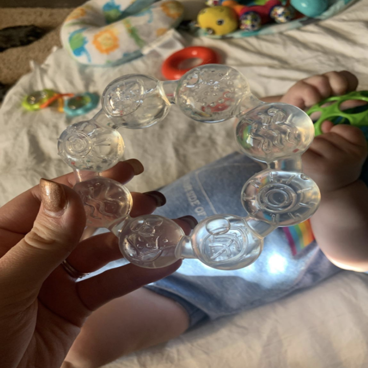 a reviewer holding up the teething ring over their baby