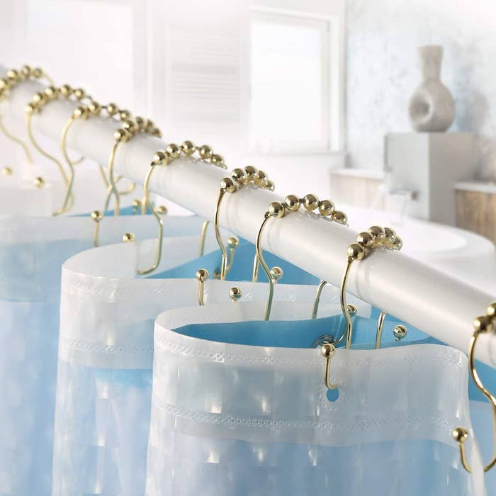 A set of gold shower hooks holding up a shower curtain
