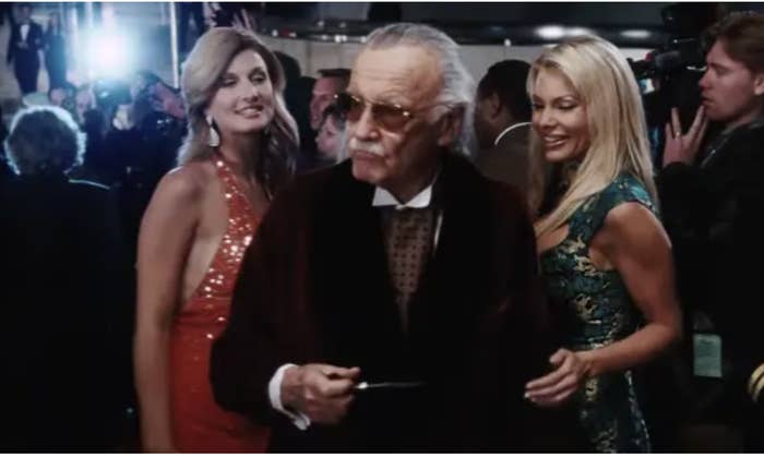 Stan Lee in a tuxedo with beautiful women on his arms