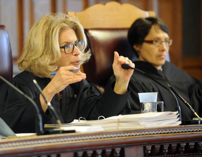 Judge DiFiore wears glasses and gestures with her hands as she speaks into a microphone from the bench in 2016.