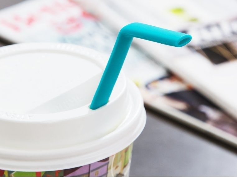 A teal straw coming out of a disposable coffee cup lid