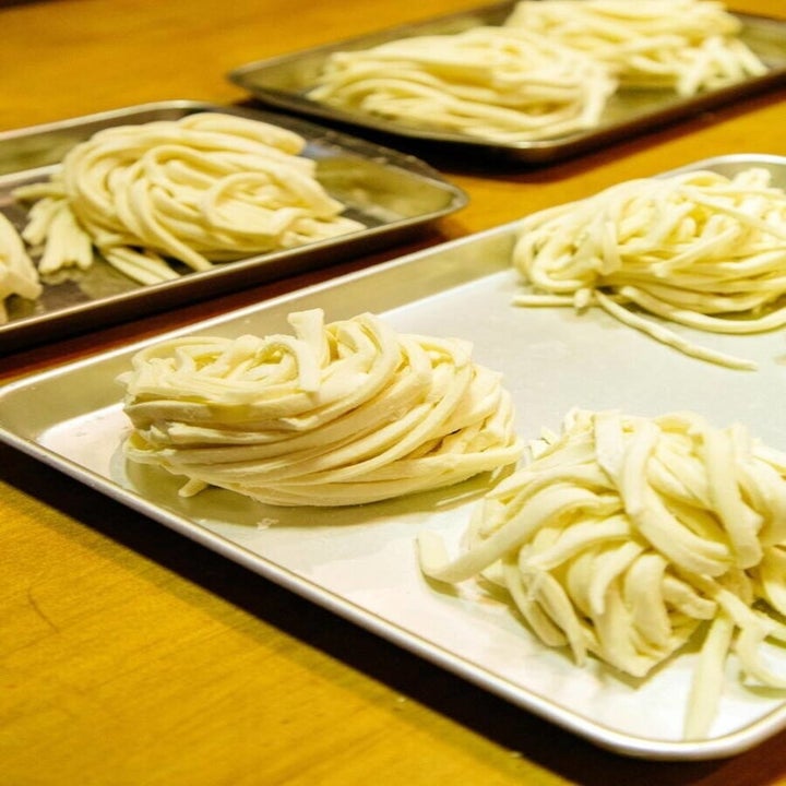 mounds of freshly cut udon noodles on trays, ready to be cooked