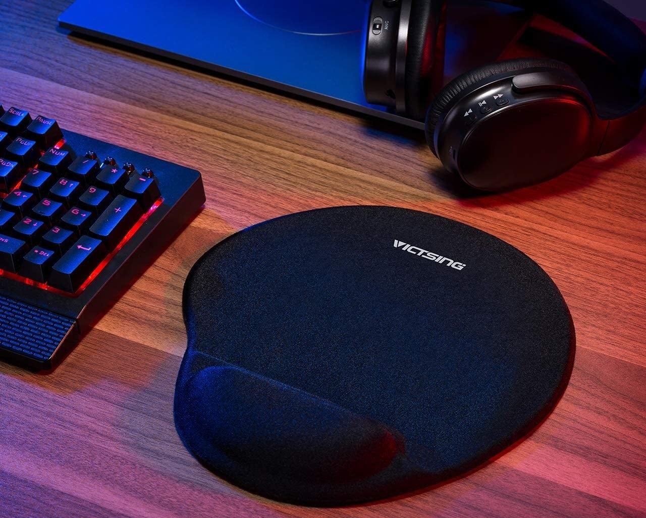 A mousepad with a wrist support on a desk beside headphones and a keyboard