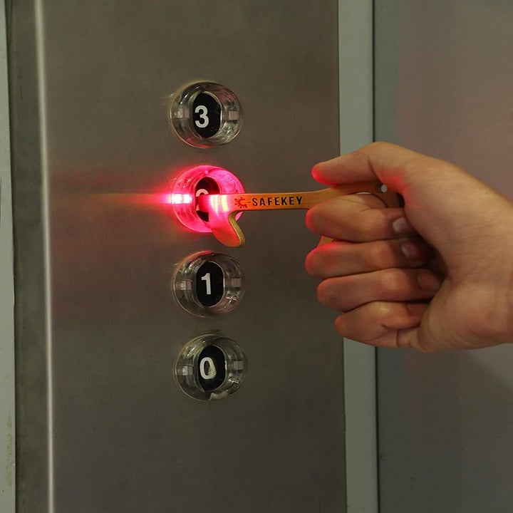 A person using the no-touch tool to press buttons in an elevator.
