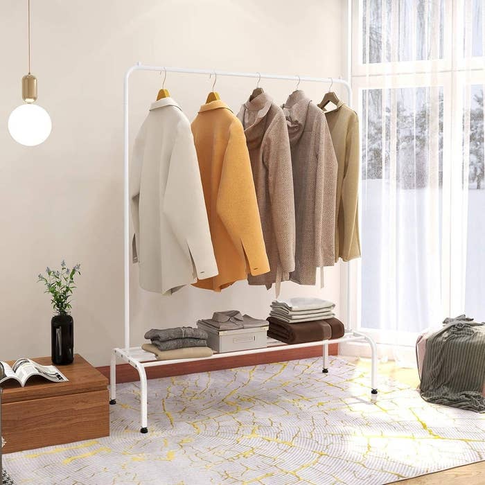 A large metal garment rack with jackets hanging from it There is shelf below that has folded clothes on it