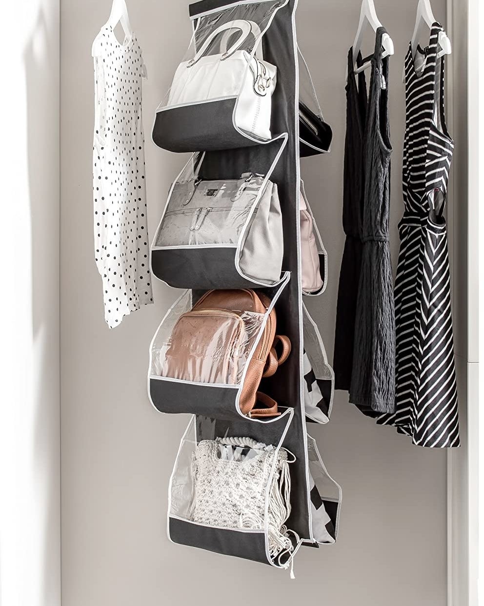 A long fabric handbag organizer hanging from a clothing rod It has four pockets on each side and are filled with large handbags