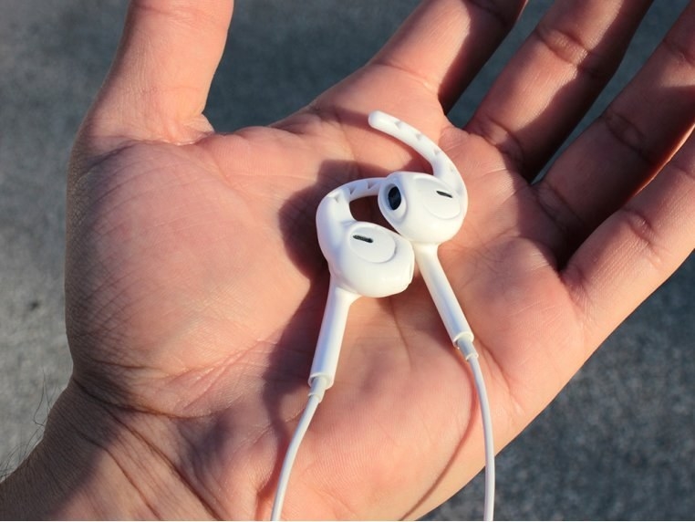 A hand holding Apple earbuds with the white hooks wrapped around them