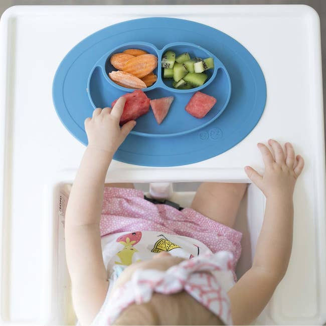top down look at oval silicone mat with walled sections for food on a baby's high chair