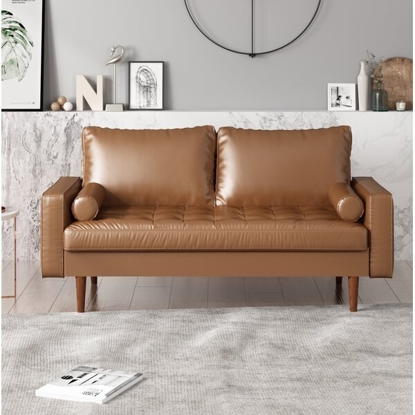 A mid-century modern sofa with rectangular back pillows, a tufted seat cushion, two rounded pillows, square arm rests, and wooden legs