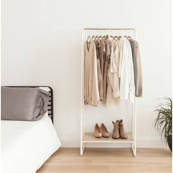 A white and natural wood clothing rack with a small shelf for about three pairs of shoes and enough hanging space for around 13 articles of clothing