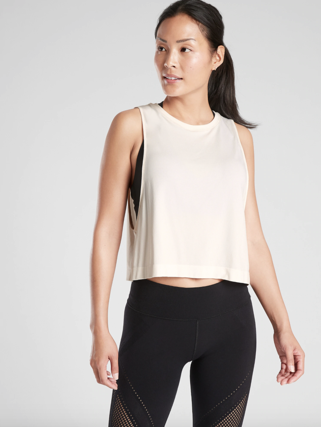 A model wearing the tank top, which stops above the waist band, and has extra wide arm holes