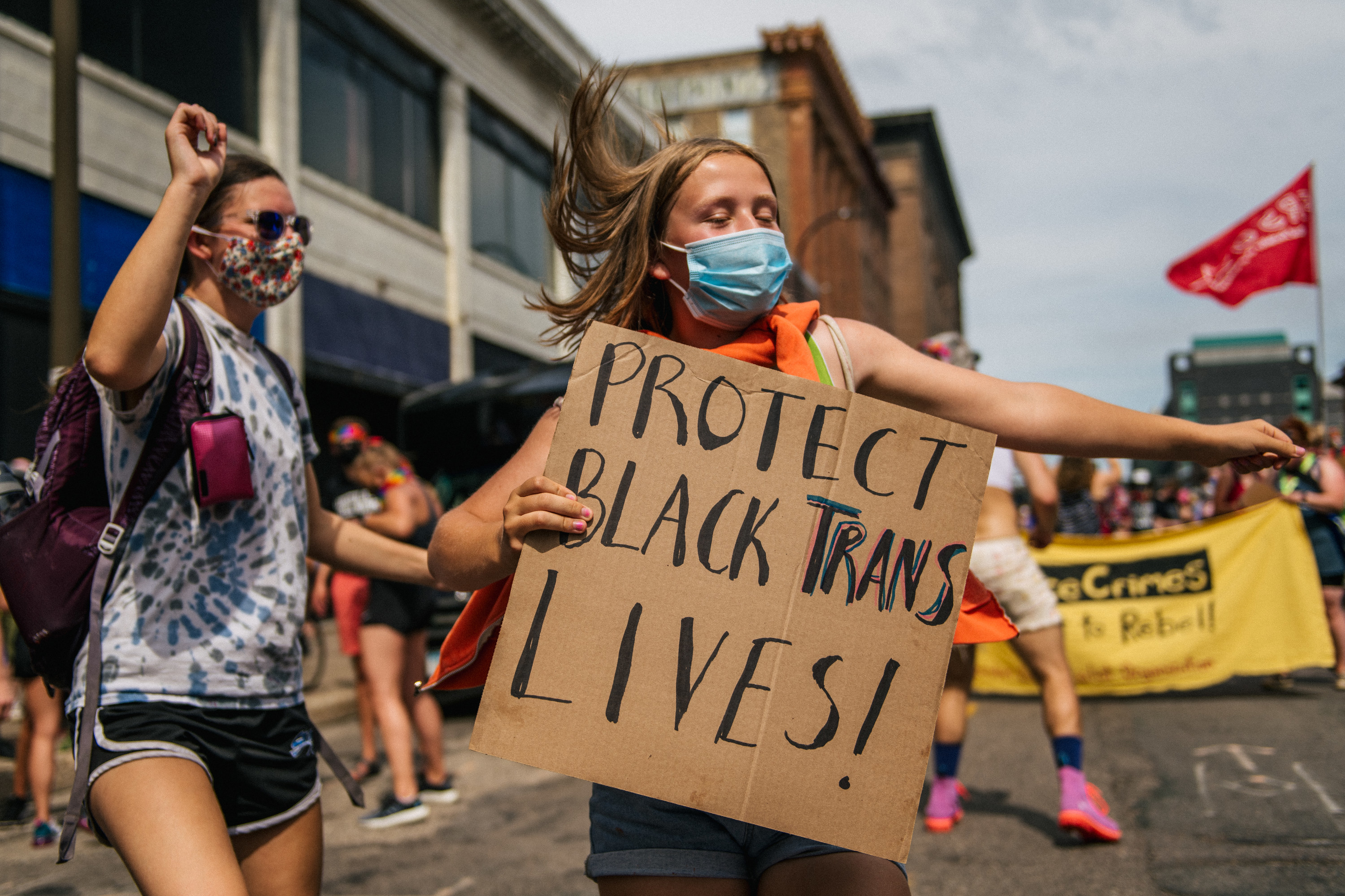 A woman dances while holding a cardboard sign that reads &quot;Protect Black Trans Lives!&quot;