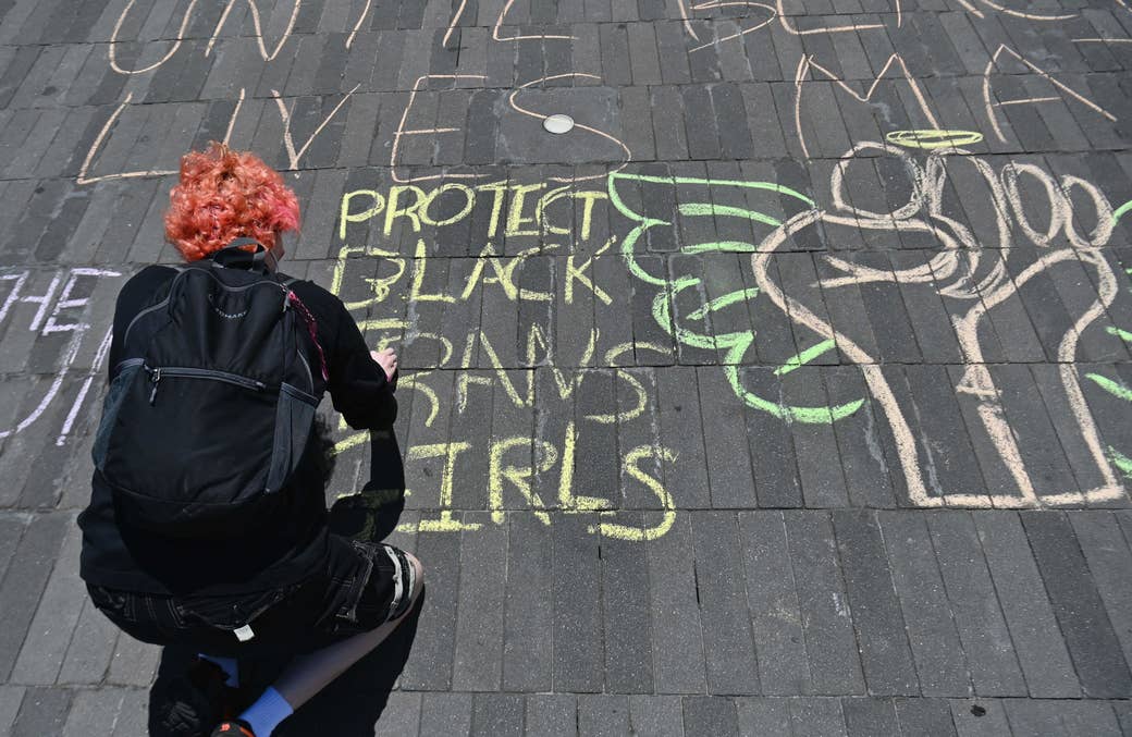 A woman writes "Protect Black Trans Girls" in chalk on a sidewalk
