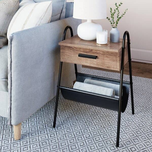 A one-drawer wooden side table with a canvas storage pouch beneath it and black metal legs