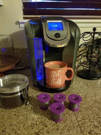 A reviewer's four purple K-cups in front of a Keurig