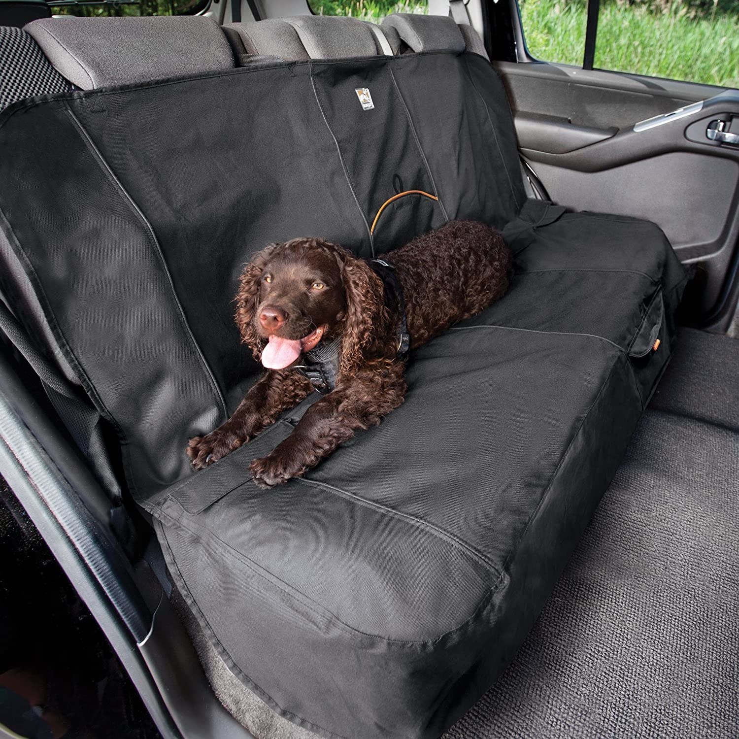 dog sits in the back of the car on top of black seat cover that sits over all three seats 