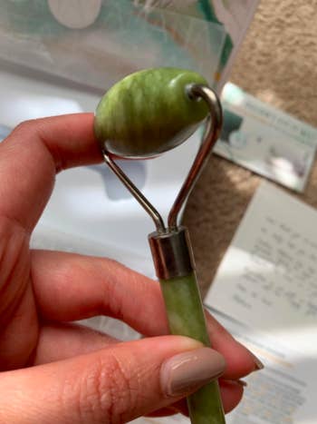 Reviewer holds green jade roller between their manicured fingers