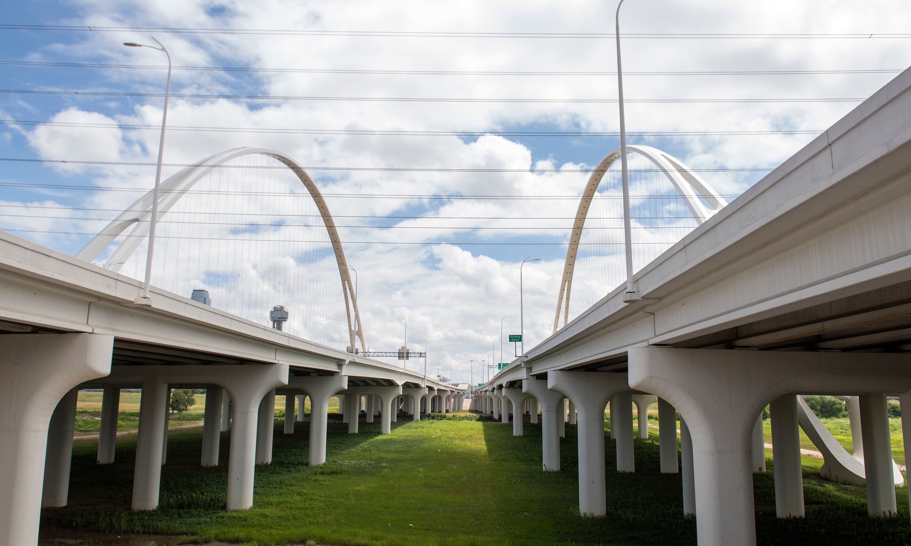Two stretches of an elevated highway above grass under a sunny sky with clouds