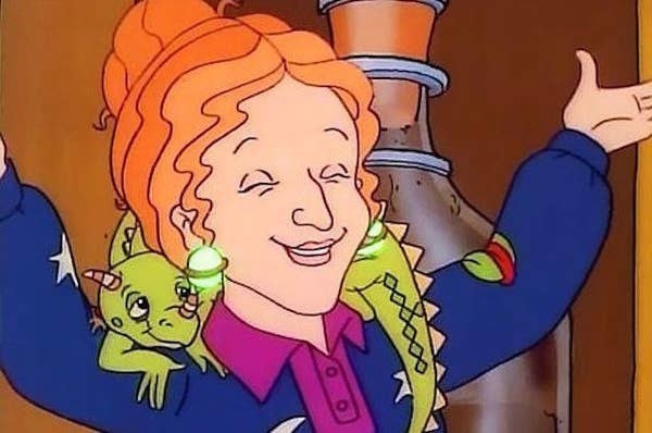 Screenshot of the cartoon Miss Frizzle smiling with her hands up, with her pet lizard, Liz, around her shoulders.