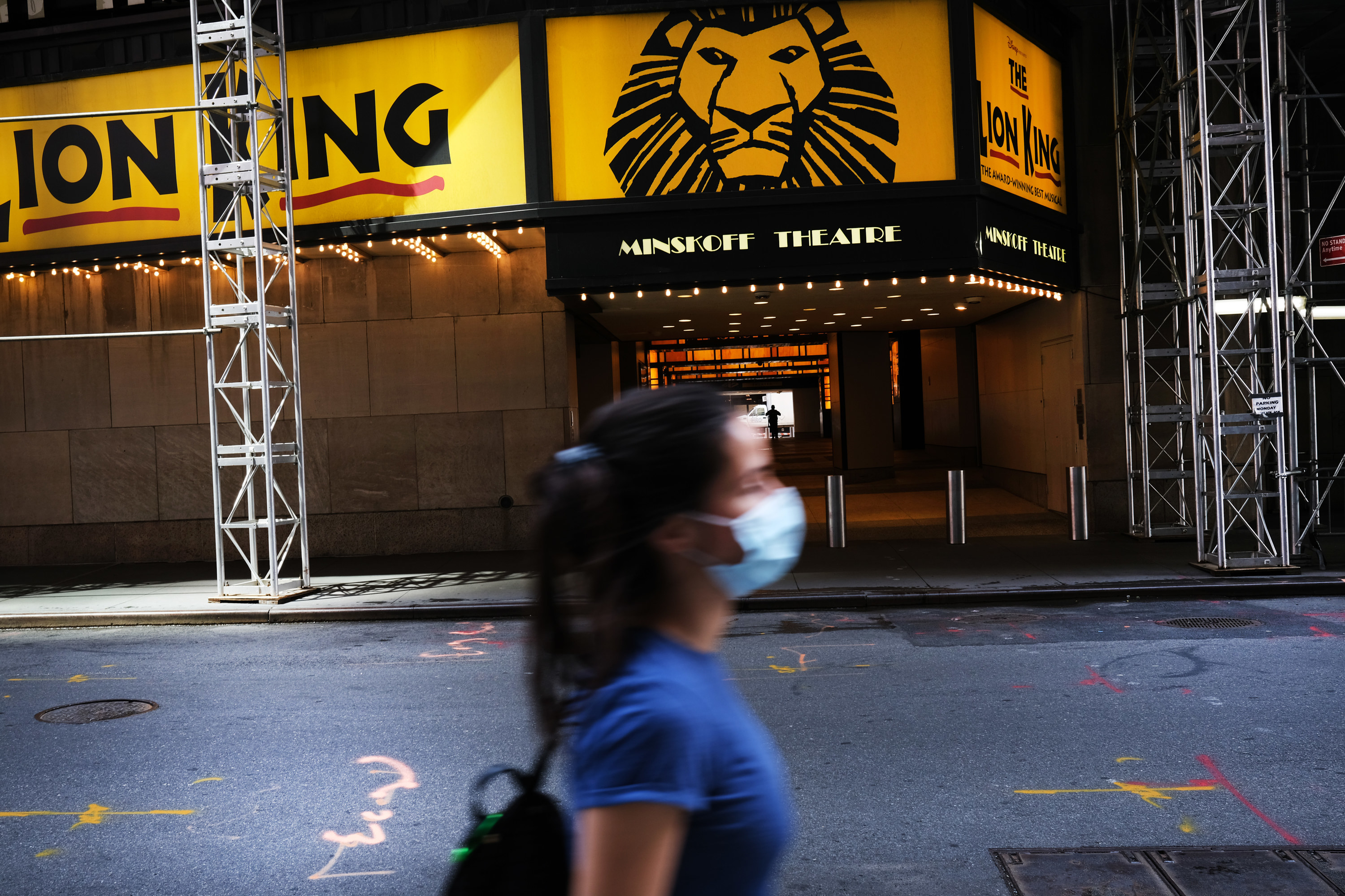 A woman wearing a face mask walks past a theater whose marquee advertises &quot;The Lion King&quot;
