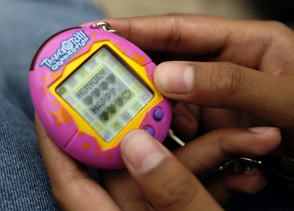 Close-up photo of a kid&#x27;s hand holding a purple Tamagotchi.