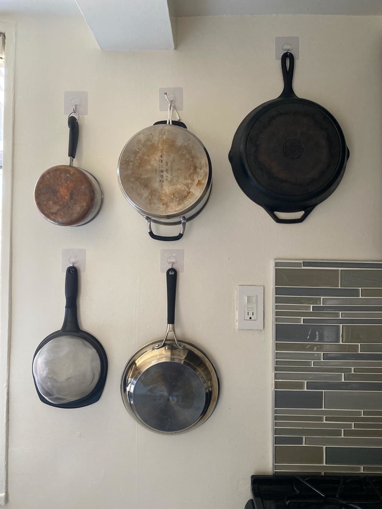 Heavy metal pots and pans hanging from reusable wall hooks