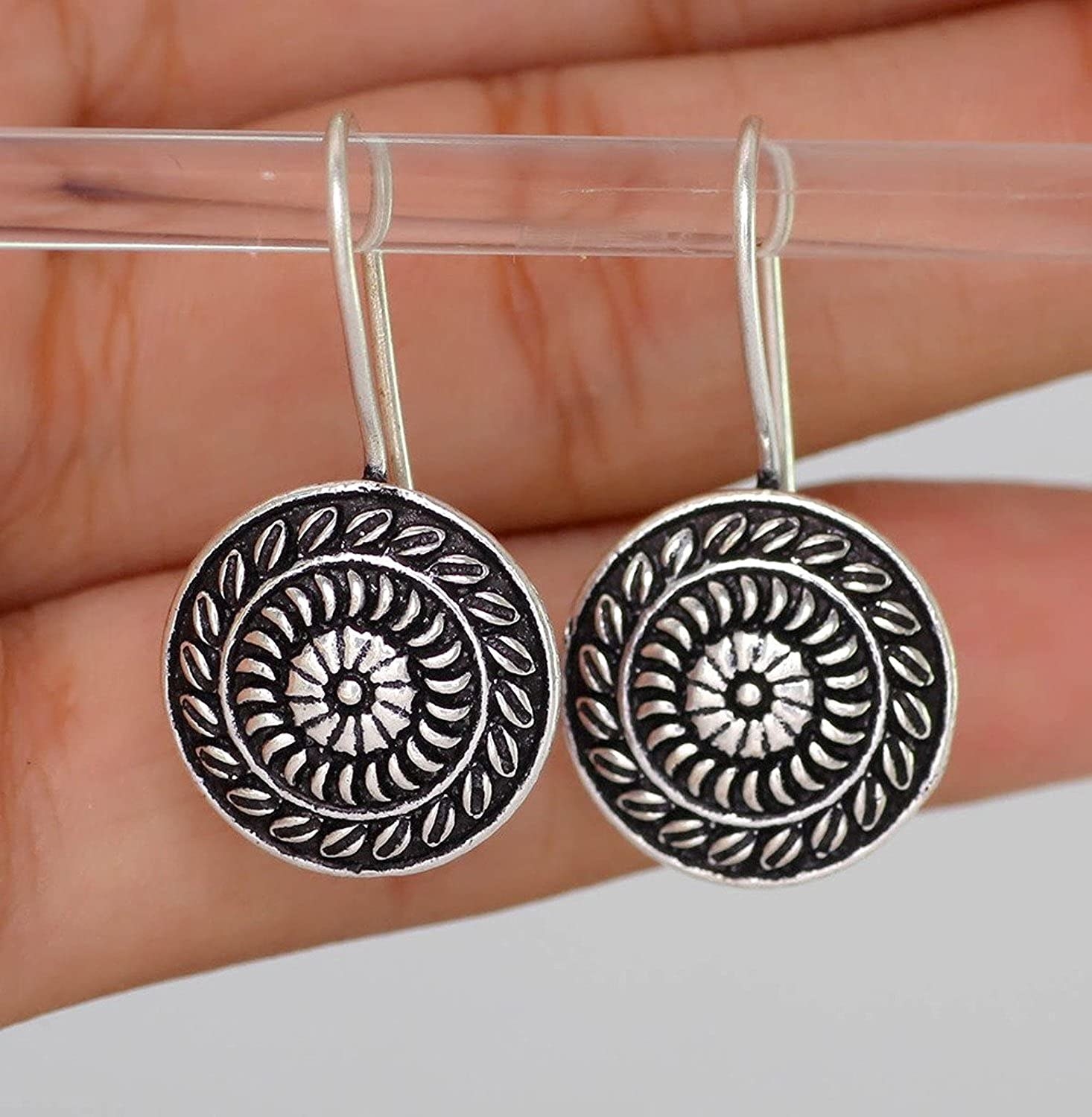 The earrings are made of oxidised silver. They are circular in shape and have spiral designs on them.