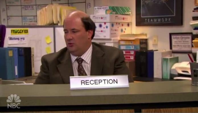 Kevin sitting at a reception desk in 'The Office'