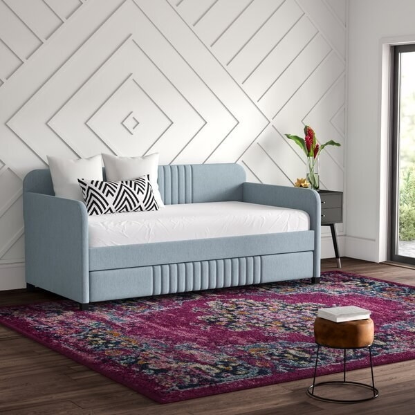 A tall trundle bed with a mattress on top and rounded edges on the back and sides. The trundle is hidden and pulled out from the bottom. 