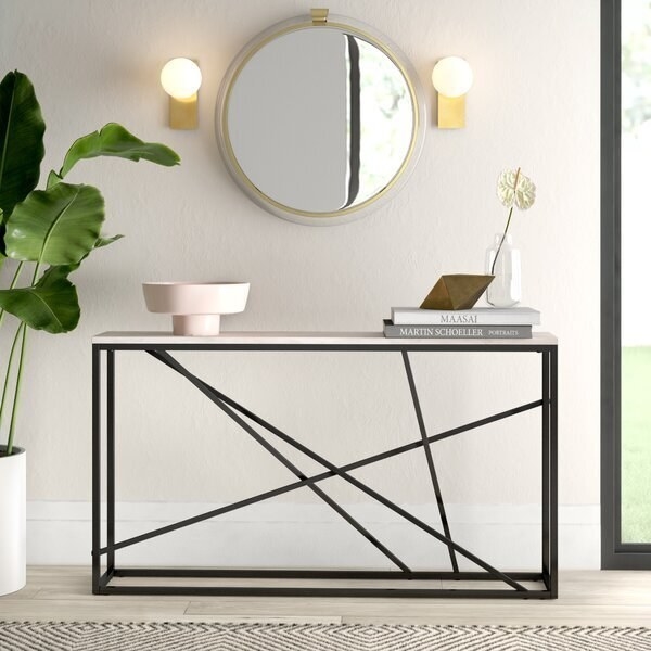 A thin, asymmetrical table with a marble table top and black metal piping in abstract designs 