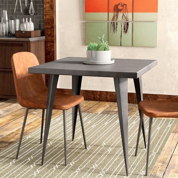 A square dining room table with legs that taper from the large triangular top to thin points at the bottom 