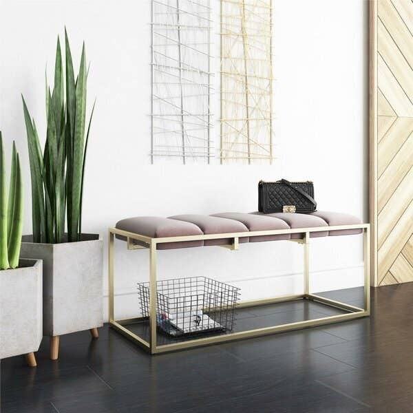 A rectangular golden bench frame with room to store things on the floor beneath and a five-cushion velvet top 