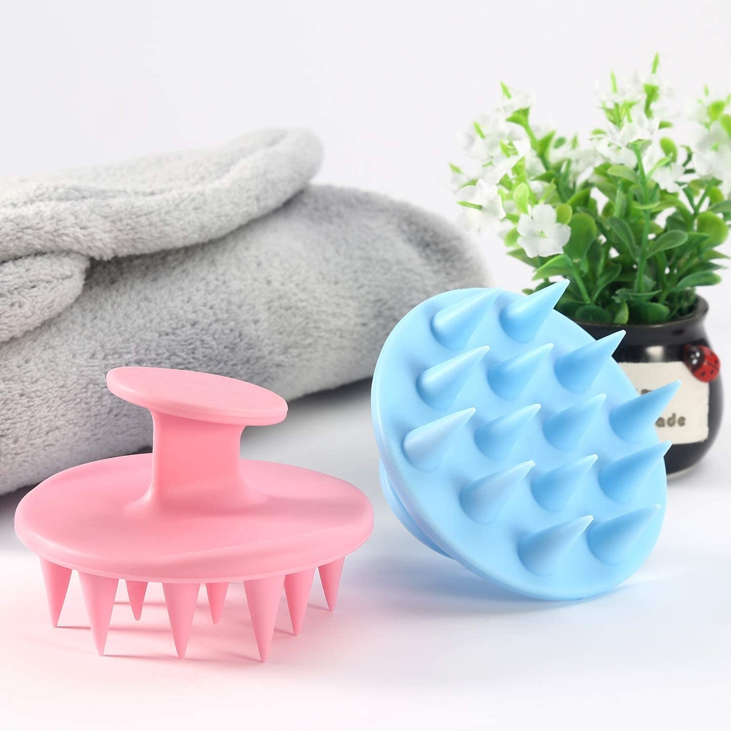 Two scalp massagers next to a towel and a plant