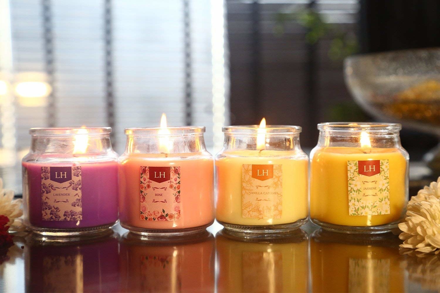 Four jars of lit aromatherapy candles of different scents on a table