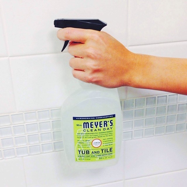 A person sprays the cleaning product onto some bath tile