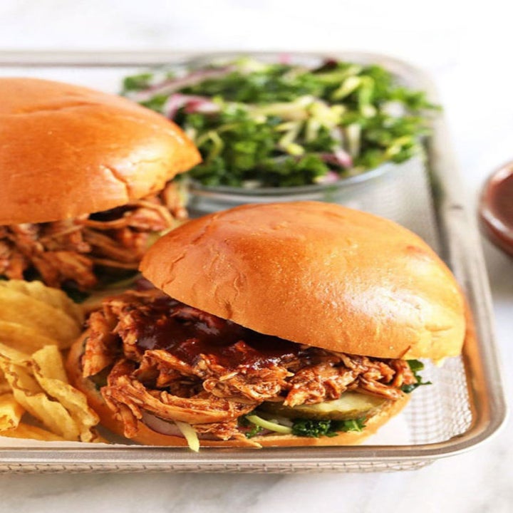 Two pulled barbecue chicken sliders with chips and salad on the side.