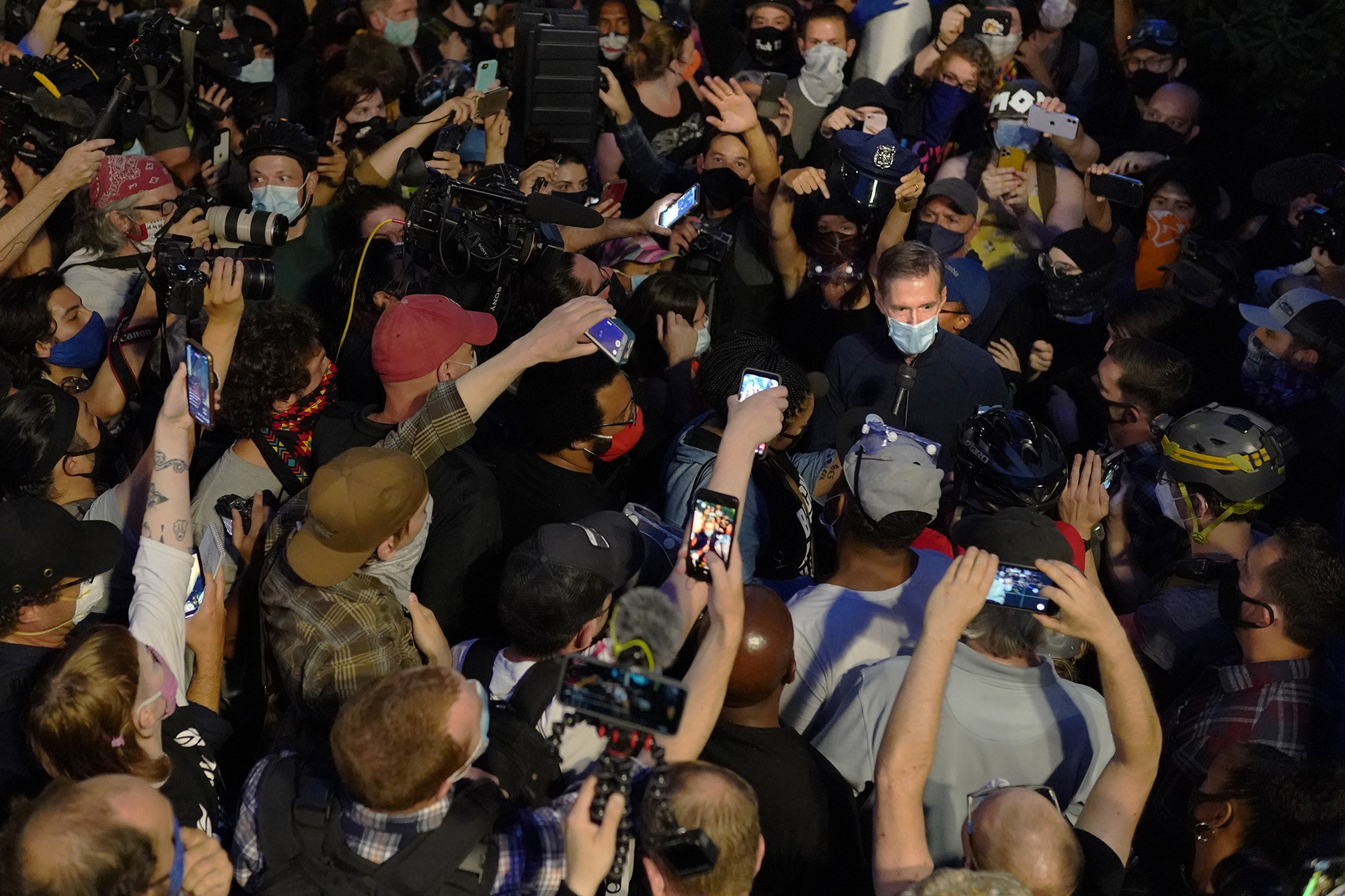 Portland Mayor Ted Wheeler is surrounded by media and protesters at a demonstration at the justice center in Portland as some hold their phones in the air