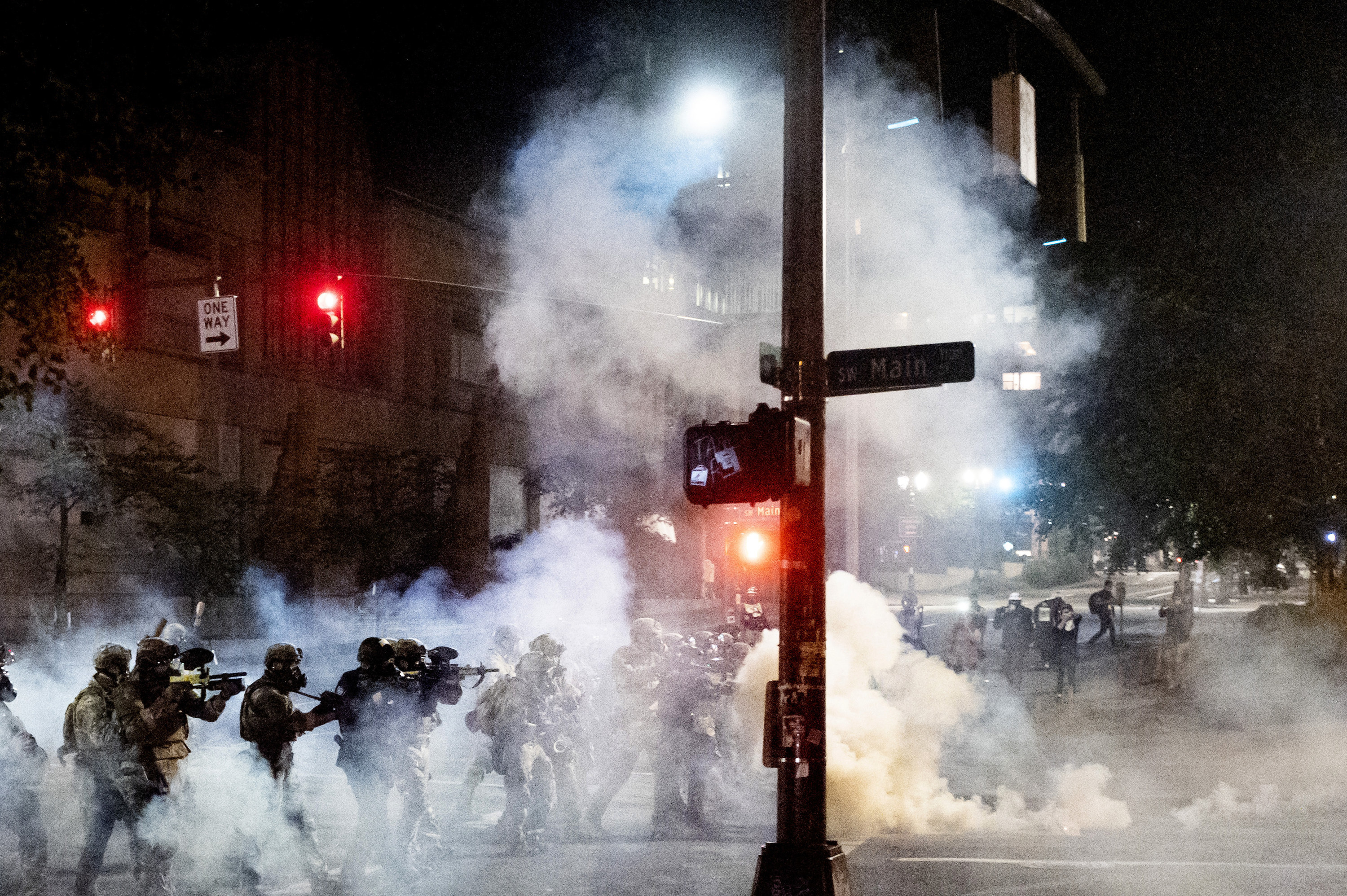 A group of federal agents walk through tear gas with crowd control munition devices that look like guns to disperse protesters