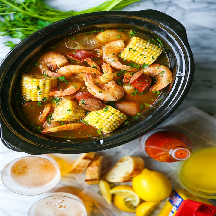 A slow cooker filled with corn on the cob, shrimp, and sausage in broth.