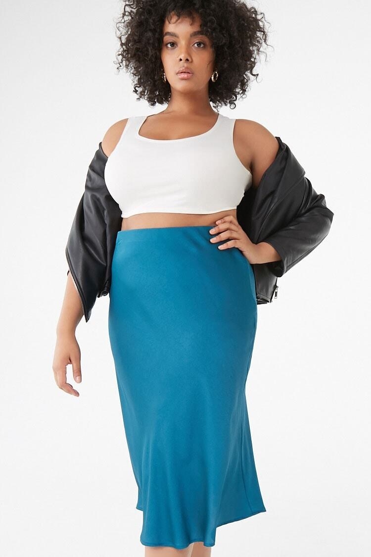 A model wearing the high-rise flowing skirt with a crop top and light jacket. The skirt hits right at the calf muscle and the top rises to the rib cage. 