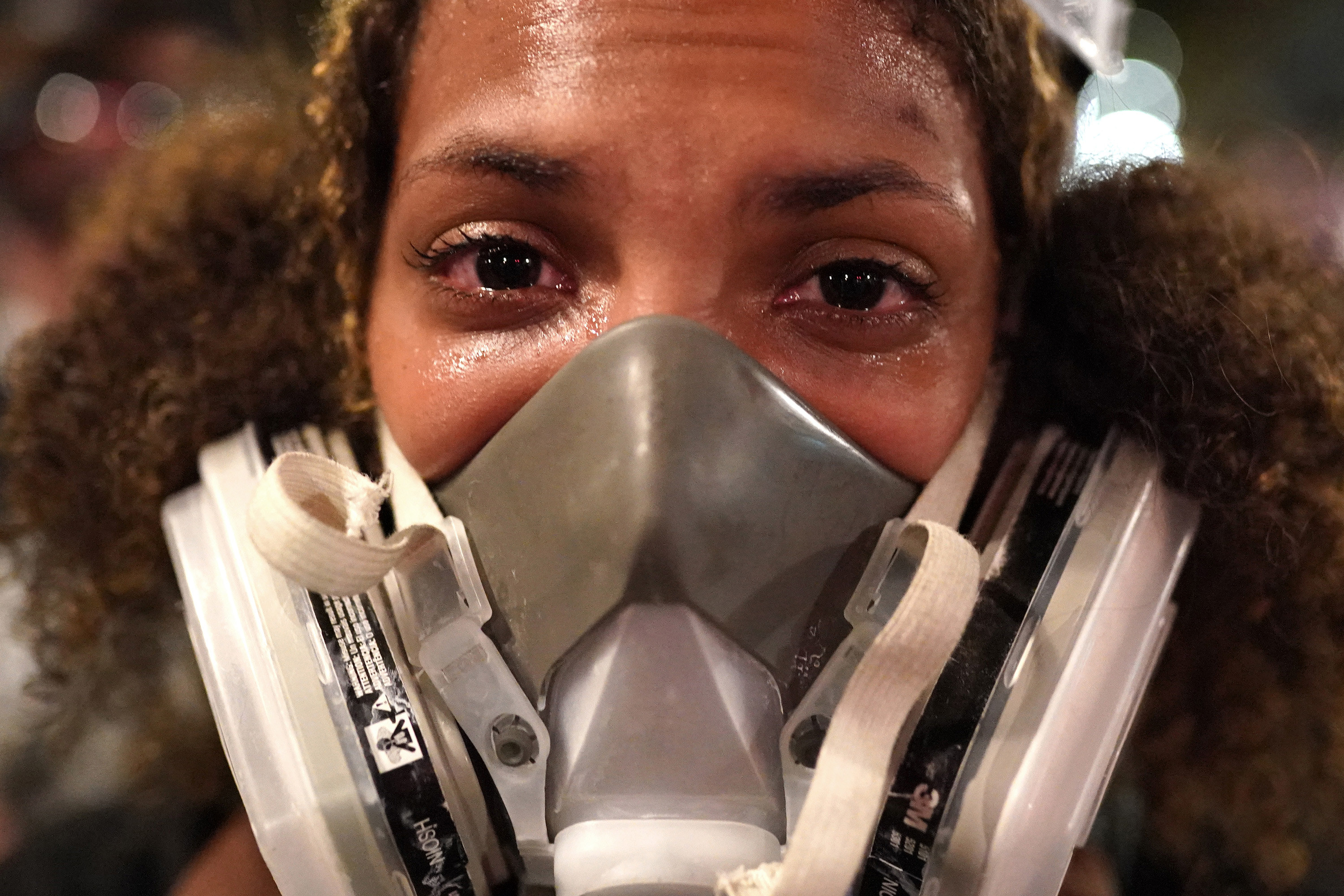 An extreme close-up of a woman wearing a mask as she reacts to tear gas and her eyes water