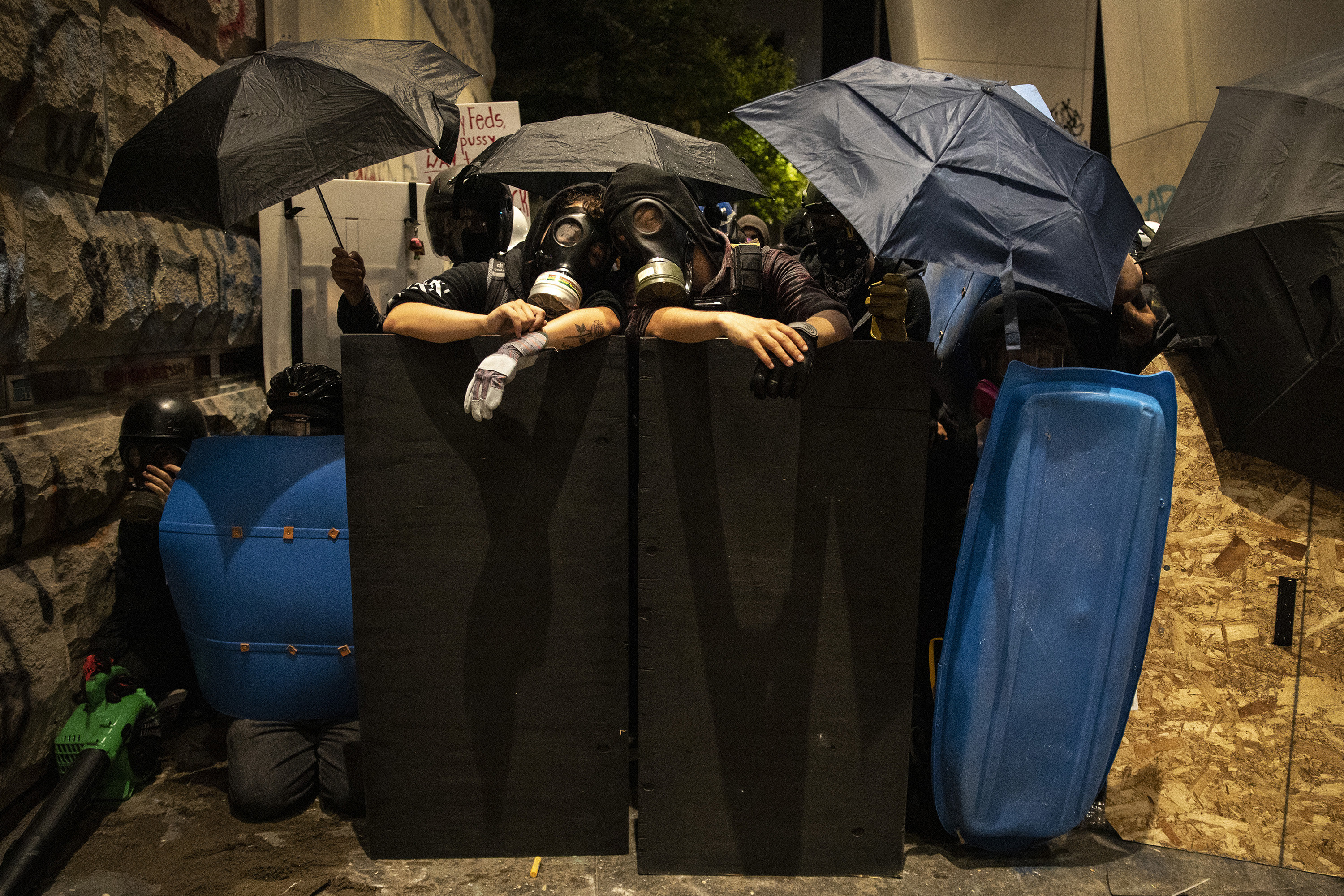 Protesters with gas masks rest against a homemade barrier during a demonstration in Portland