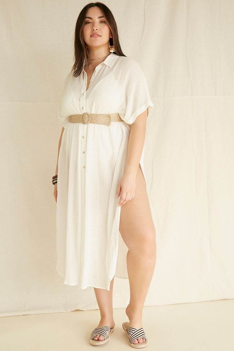 A model wearing the sheer, flowing dress and exposing their leg to show the thigh-high slit on the side. The shirt has short sleeves, a collar, and buttons from the top of the collar to the center of the stomach. 