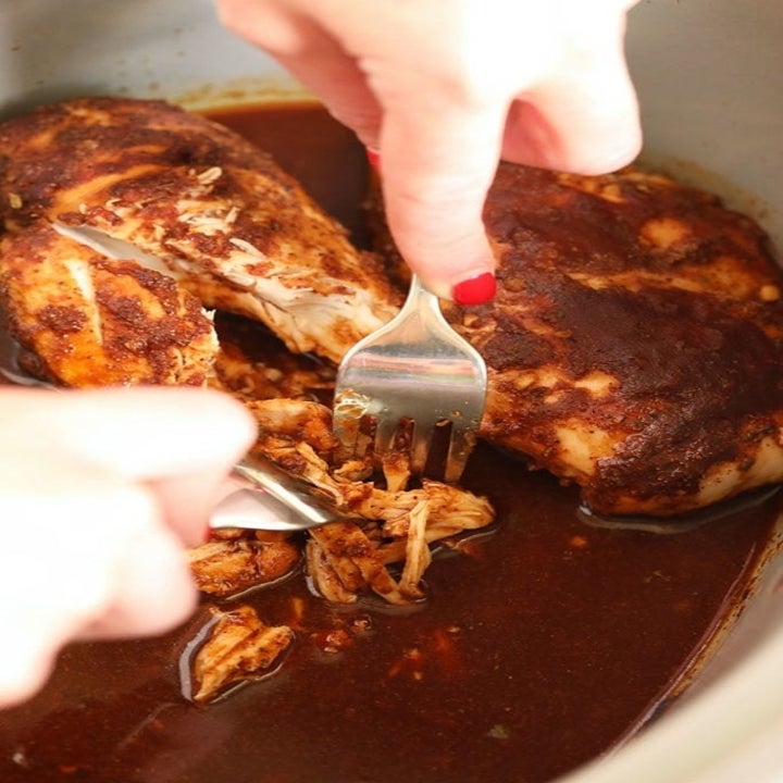 Someone shredding barbecue chicken breasts in the slow cooker with two forks.